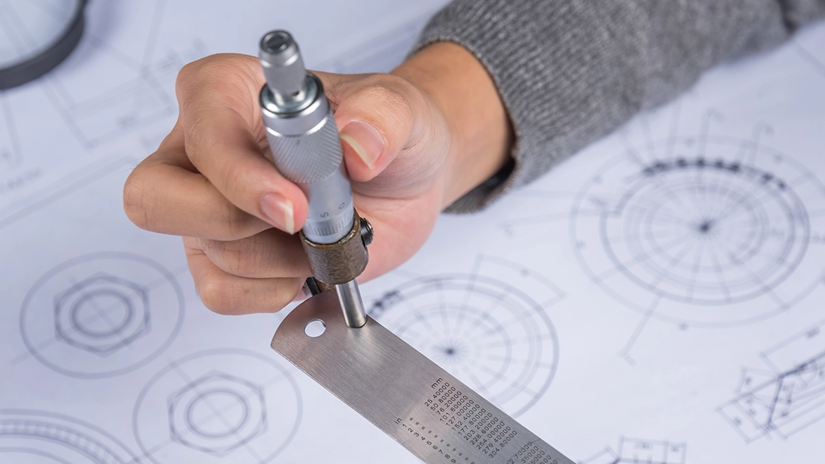 Measuring a part with a micrometer over a technical drawing